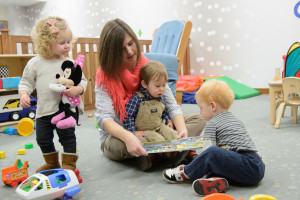 Three toddlers listen to a book being read by the Children's Learning and Care Center staff member