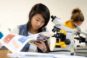 woman works in a biology lab with a lab manual and a microscope