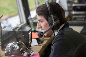 Student sits in booth at football came broadcasting game in a headset microphone